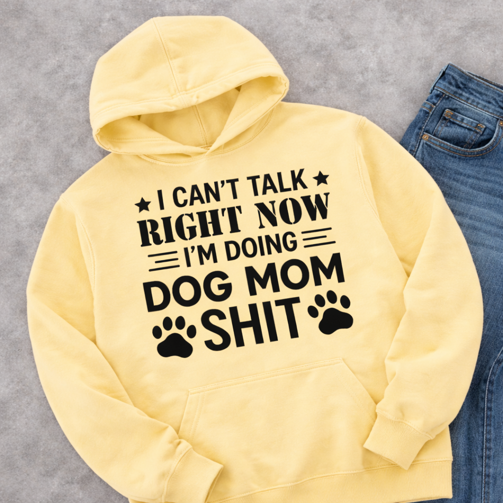 Yellow dog mom hoodie mockup with bold statement “I Can’t Talk Right Now I’m Doing Dog Mom Shit” printed in black lettering, styles beside blue denim jeans on a neutral background.