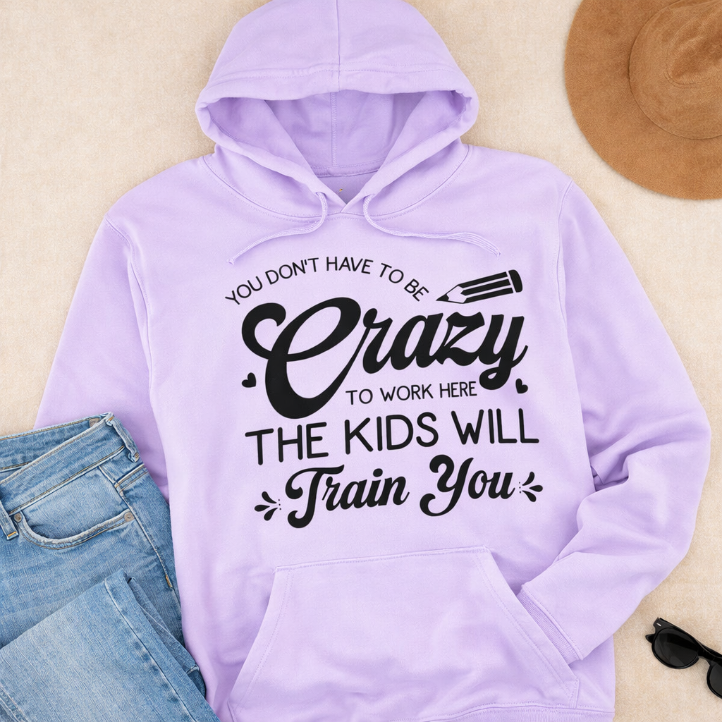 Light purple hoodie with “You don’t have to be crazy the kids will train you” SVG design in black, flat lay with jeans, hat, and sunglasses on neutral background – Funny Teacher SVG Quotes