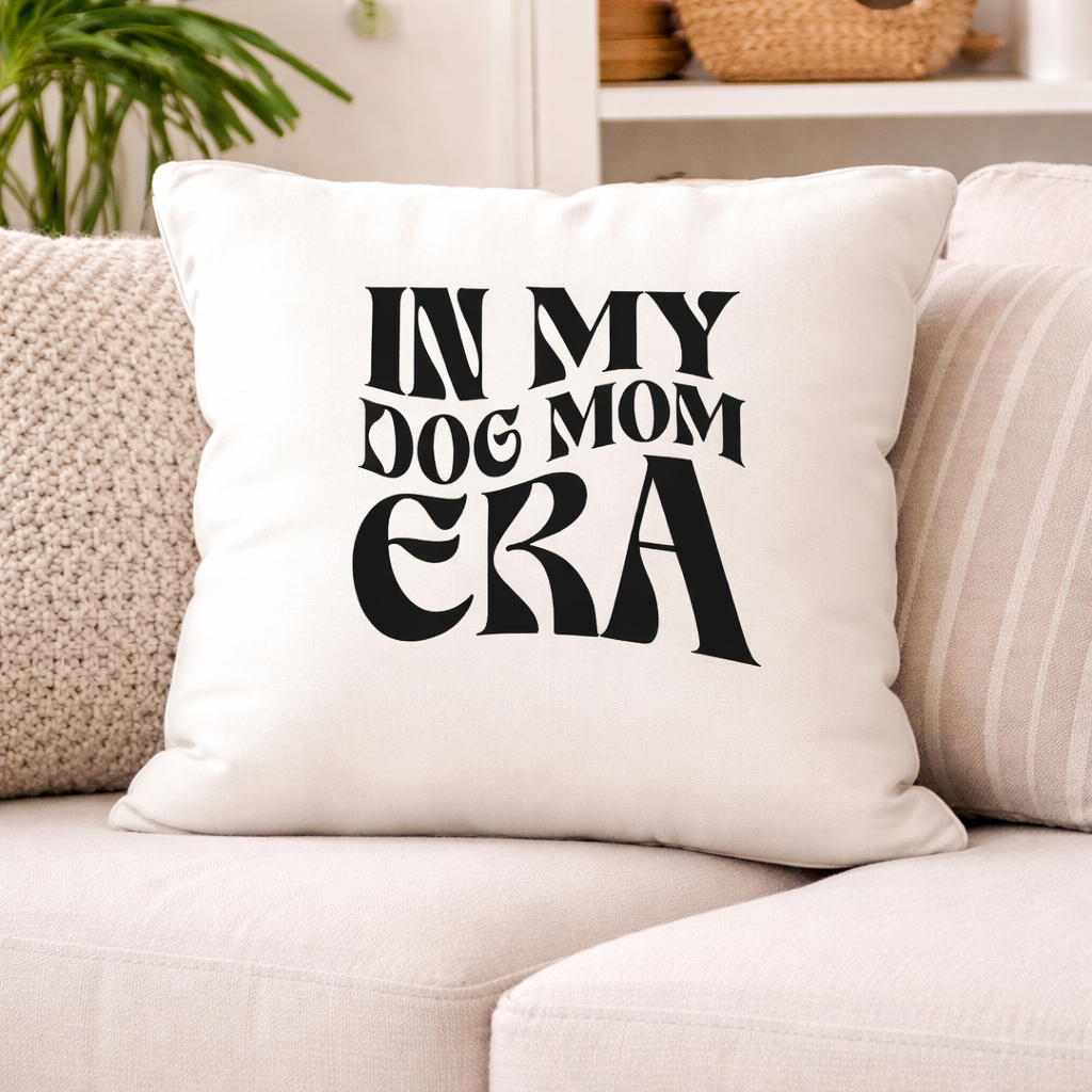 Decorative pillow with In My Dog Mom Era SVG design in black lettering, placed on cozy sofa in neutral home interior