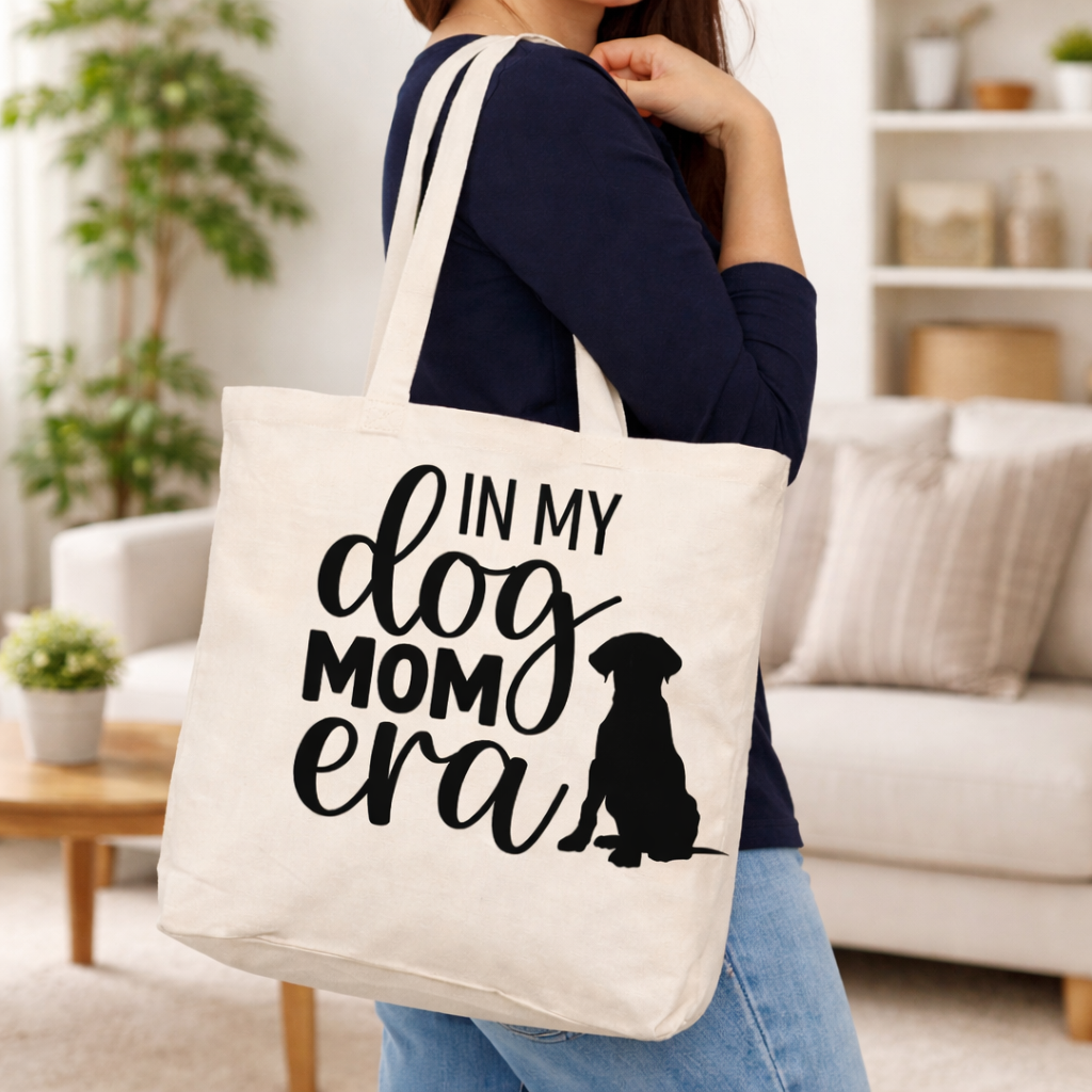 Beige tote bag with In My Dog Mom Era SVG design and dog silhouette, carried by woman in cozy home interior