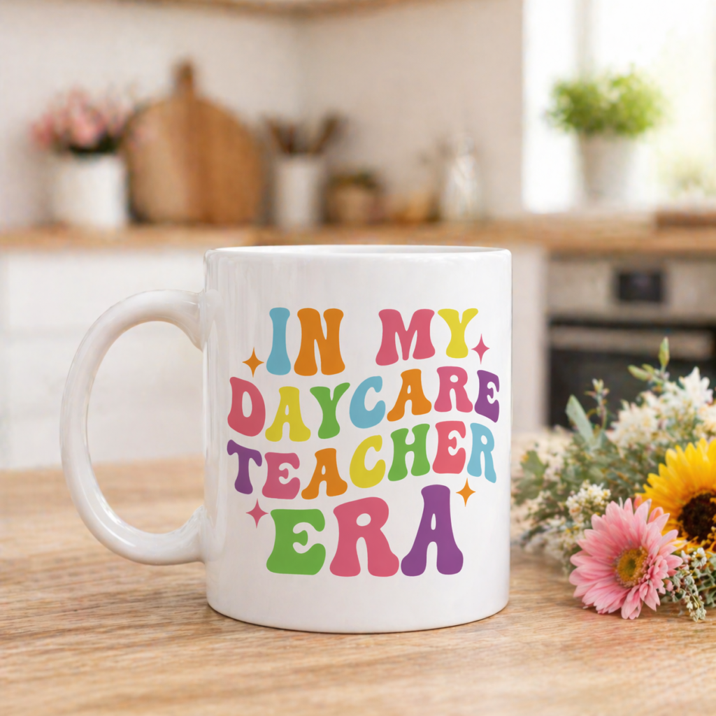 White mug with In My Daycare Teacher Era colorful retro lettering placed on wooden table with flowers in soft kitchen background